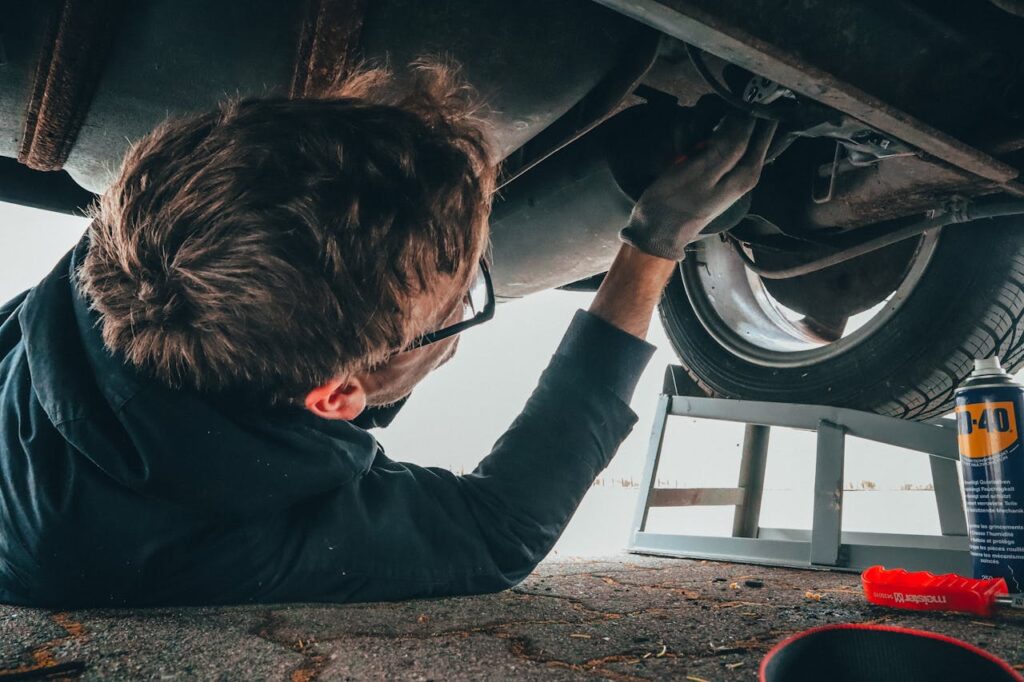 pexels-photo-2244746 Mechanic skillfully repairing car undercarriage in outdoor setting with tools.