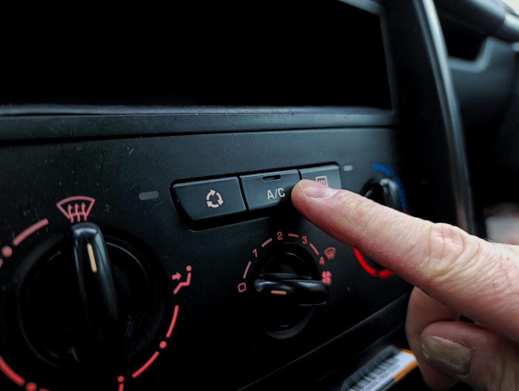 pexels-photo-30684554-30684554 Close-up of a person adjusting a car's air conditioning system inside a vehicle cabin.